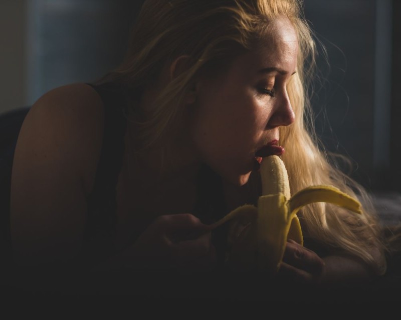 una mujer simula sexo oral con un plátano en la cama