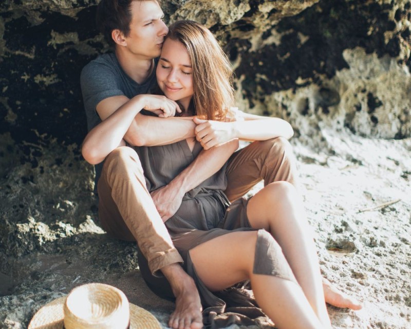 pareja se abraza en la playa al atardecer detrás de una roca