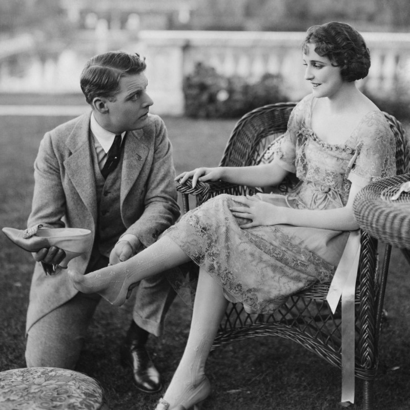 Fotografía en blanco y negro de hombre poniendo zapato a mujer años 20