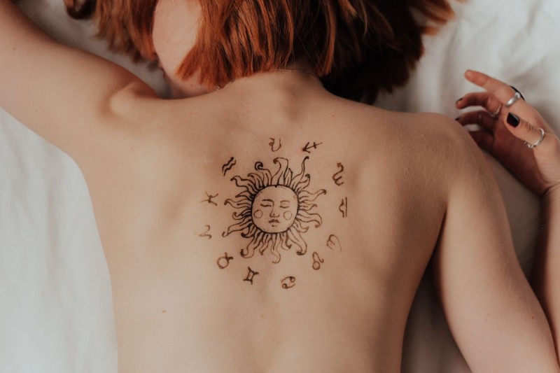 woman lying on bed, bare back, with tattoo of zodiac signs